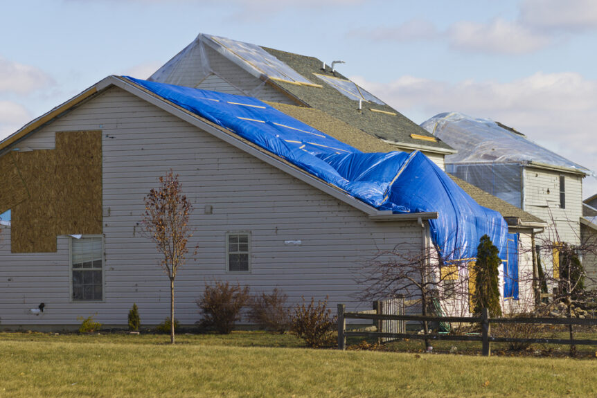 home damaged by storm with blue tarp over roof and siding missing