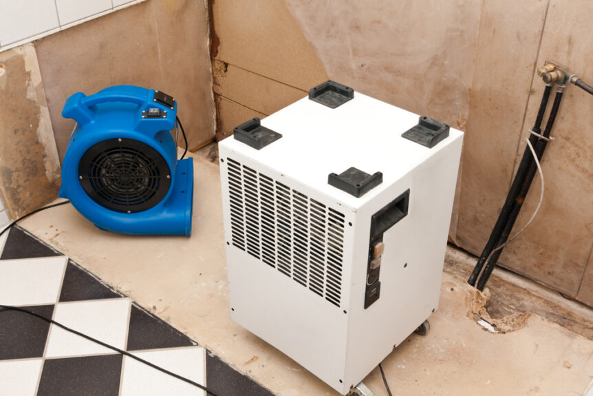 professional water damage restoration air mover and dehumidifier drying out room damaged by water