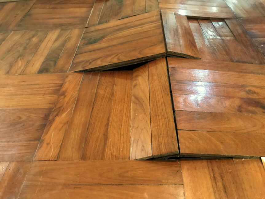 older wood floors that have buckled due to water damage and moisture inside house